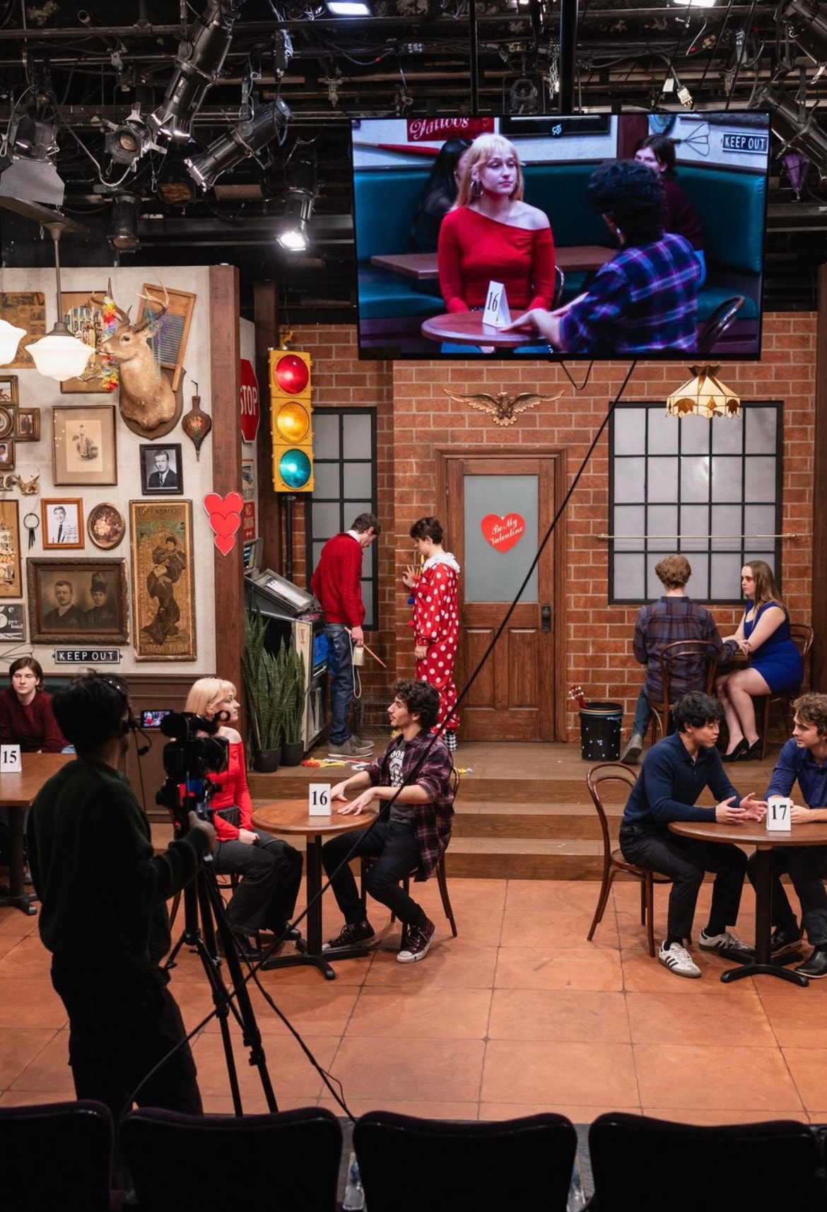 Lex Leone on TV studio set in red top with full production crew and cast