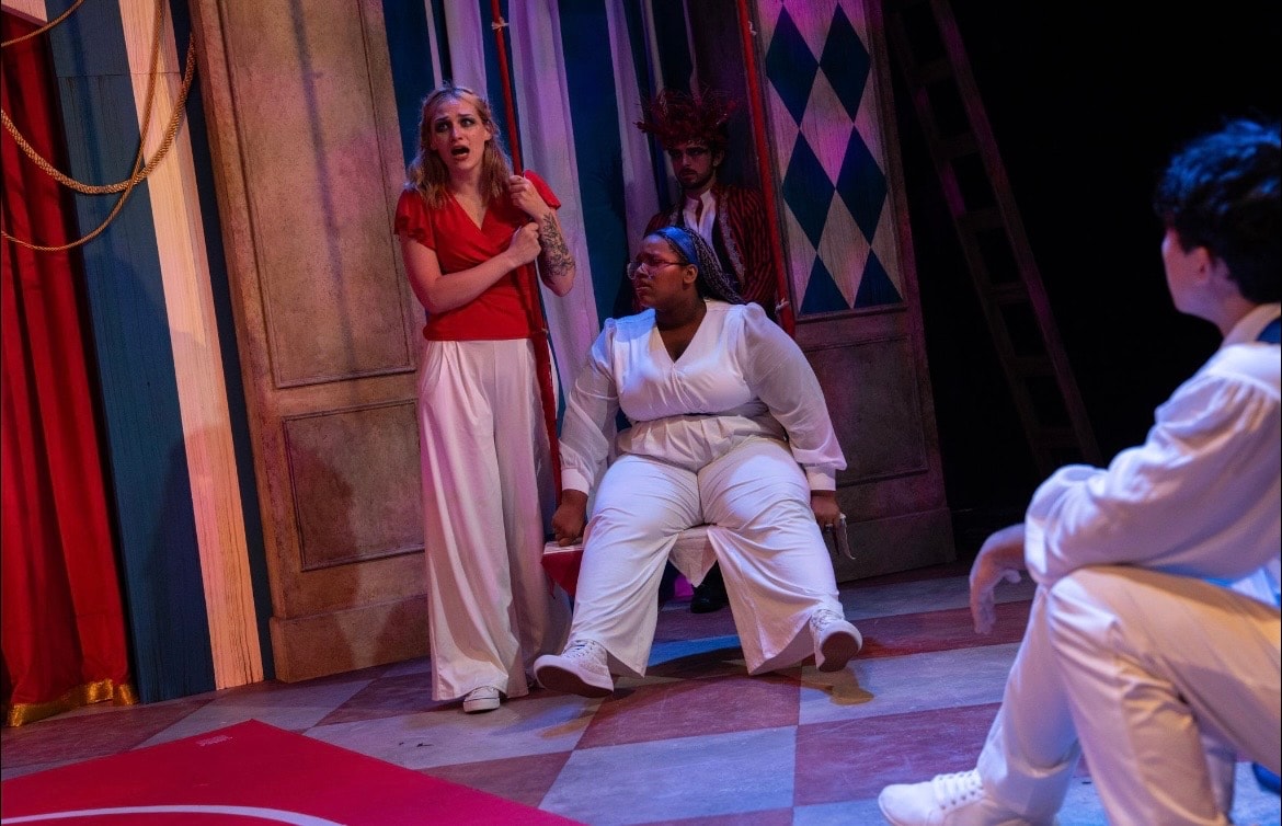 Lex Leone on stage in red top with ensemble cast