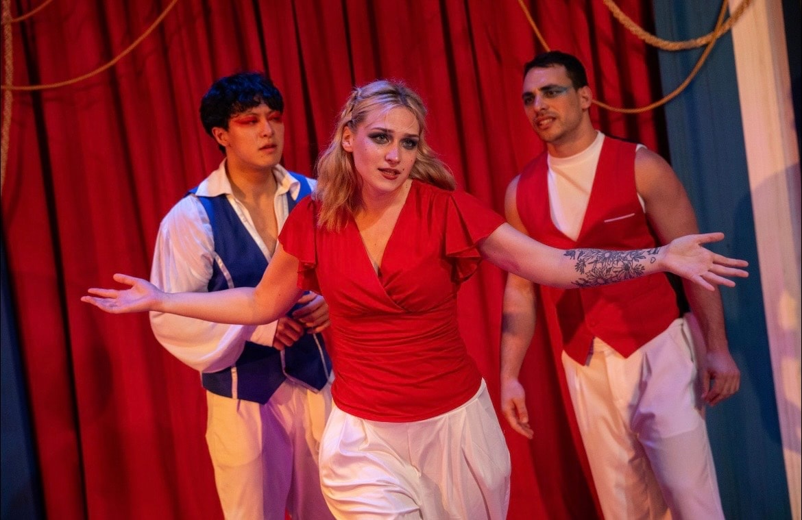 Lex Leone on stage in red top arms outstretched with co-stars