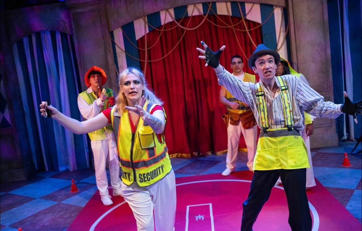 Lex Leone on stage in security vest with ensemble cast