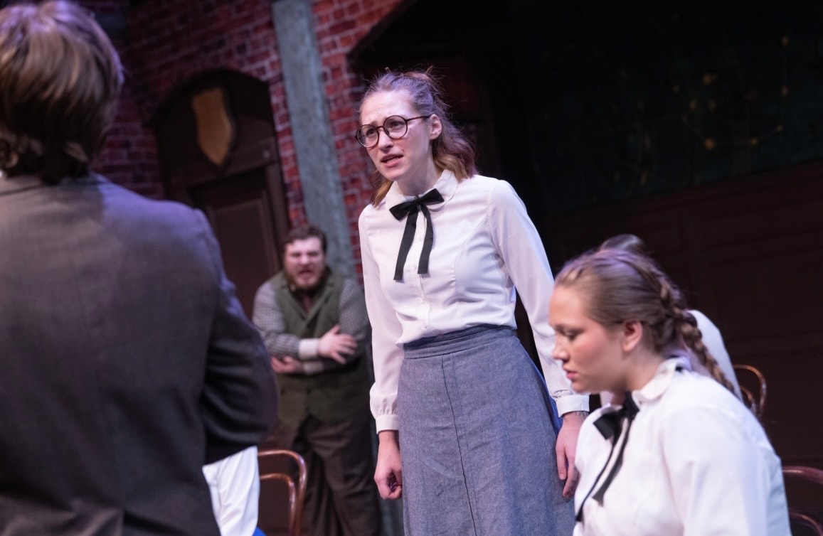 Lex Leone on stage in white blouse confronting co-stars