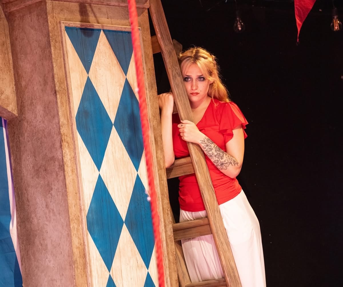 Lex Leone on stage in red top on ladder